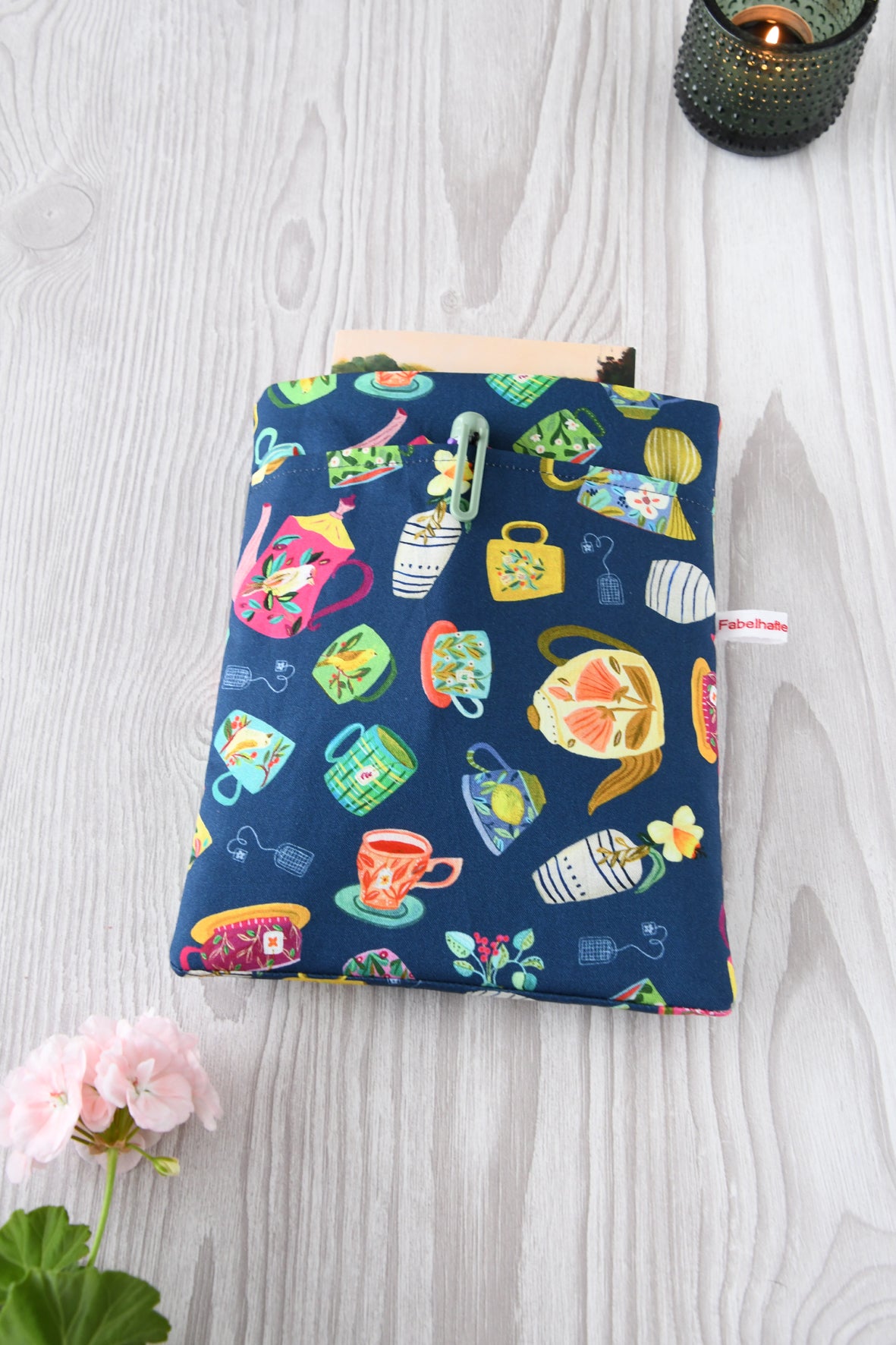 Handgenähte Buchtasche „Teatime“ mit bunten Teetassen auf blauem Baumwollstoff. Zu sehen ist das Hauptfach und die praktische Vordertasche über die gesamte Breite für Stifte und Lesezeichen.