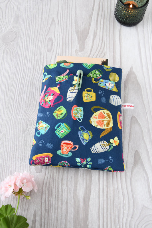 Handgenähte Buchtasche „Teatime“ mit bunten Teetassen auf blauem Baumwollstoff. Zu sehen ist das Hauptfach und die praktische Vordertasche über die gesamte Breite für Stifte und Lesezeichen.