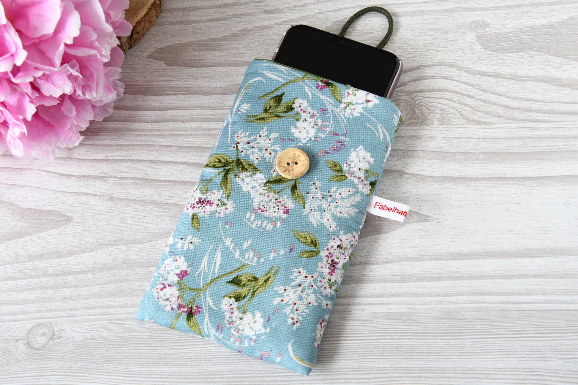 Geöffnete Stoff-Handyhülle mit Blumenmuster und einem Smartphone, das darin sicher vor Kratzern geschützt wird.