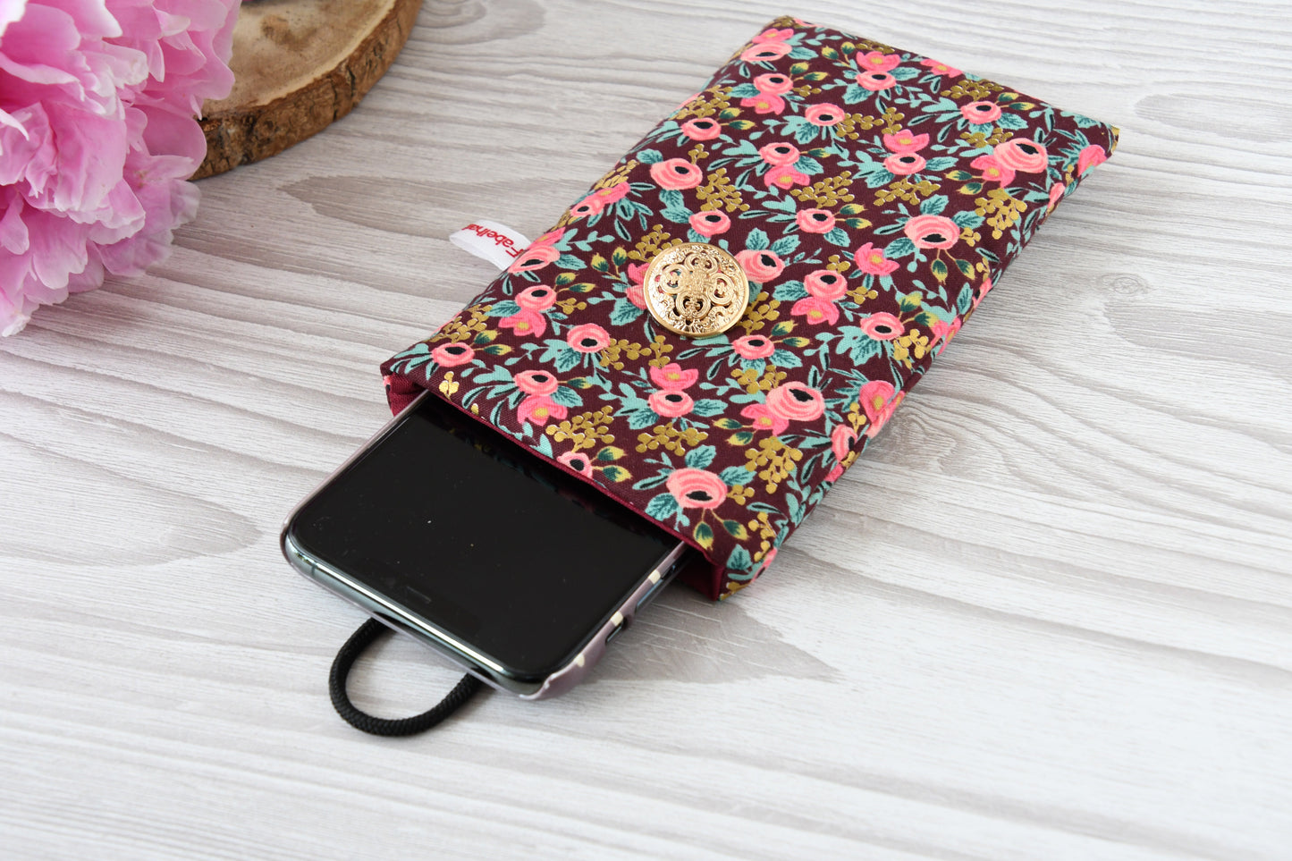 Geöffnete Stoff-Handyhülle mit Blumenmuster und einem Smartphone, das darin sicher vor Kratzern geschützt wird.