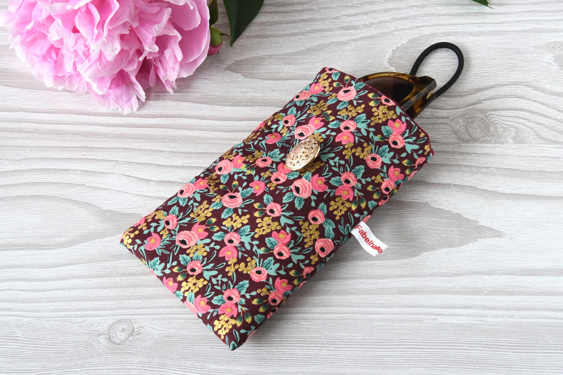 Geöffnete Stoff-Handyhülle mit Blumenmuster und einer Sonnenbrille, das darin sicher vor Kratzern geschützt wird.