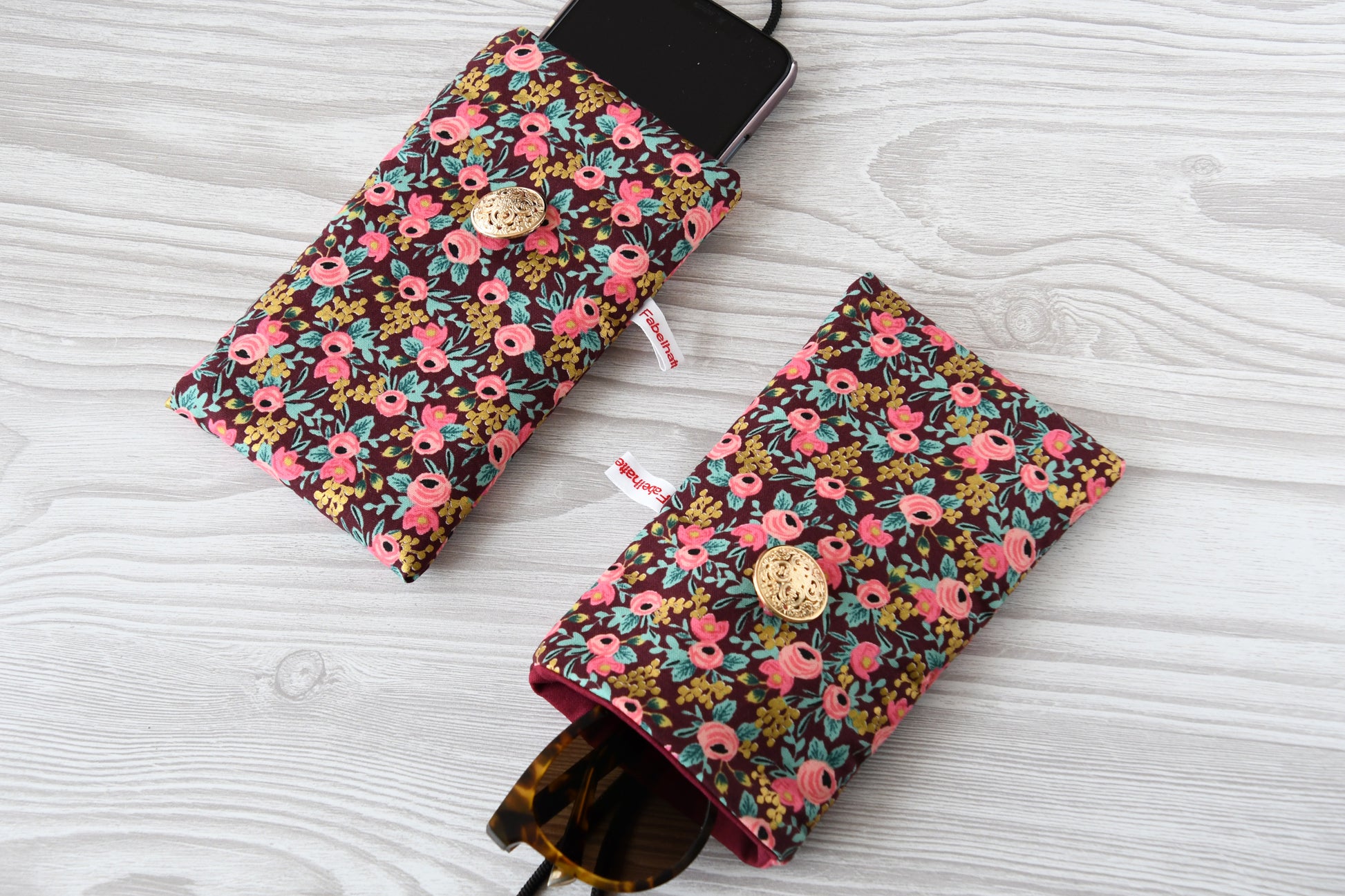 Zwei weich gepolsterte Alltagshelfer von Fabelhafte Werkstatt im Vergleich: Handytasche mit Smartphone und Brillenetui mit Sonnenbrille nebeneinander liegend.