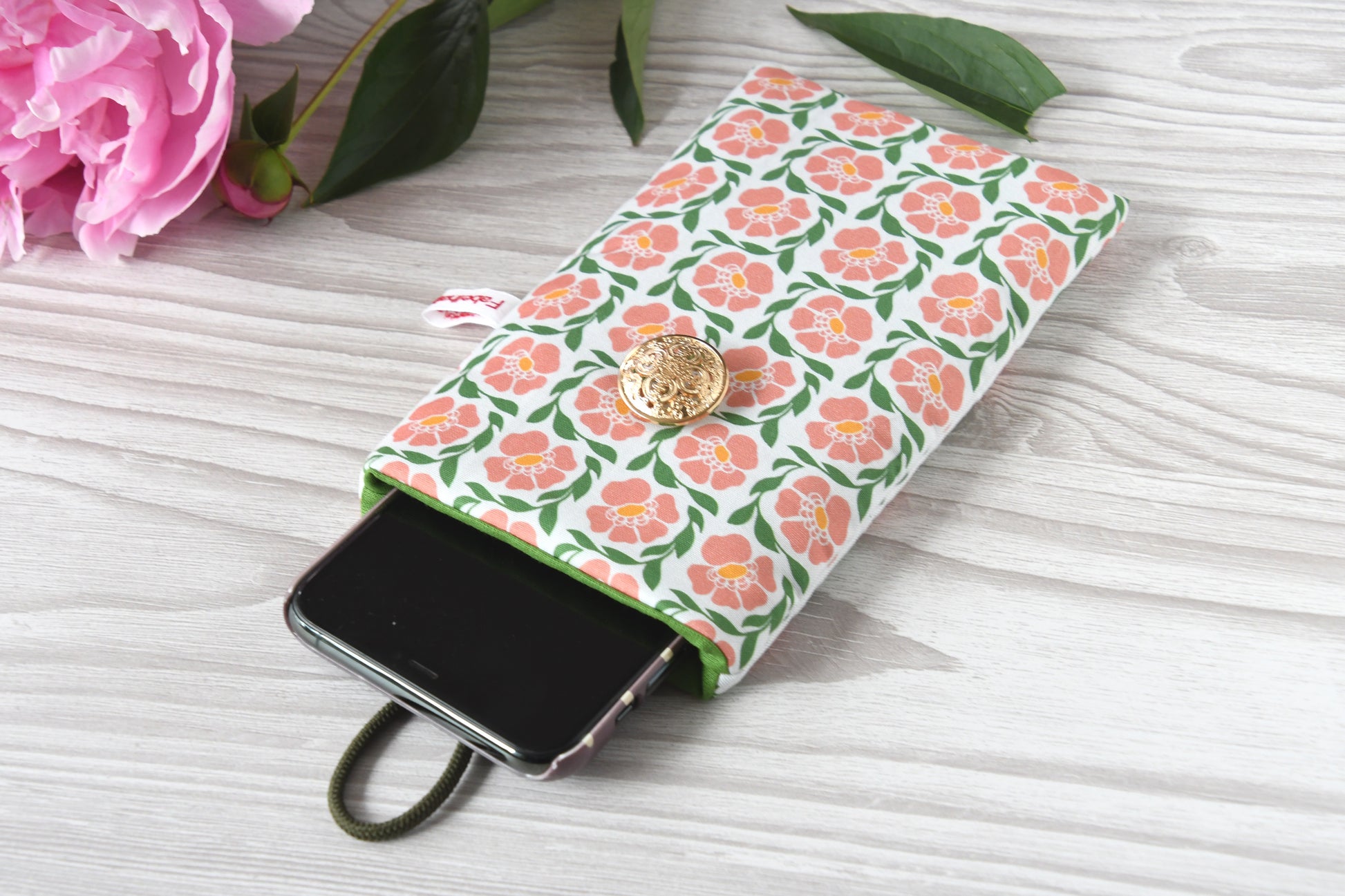 Geöffnete Stoff-Handyhülle mit Blumenmuster und einem Smartphone, das darin sicher vor Kratzern geschützt wird.