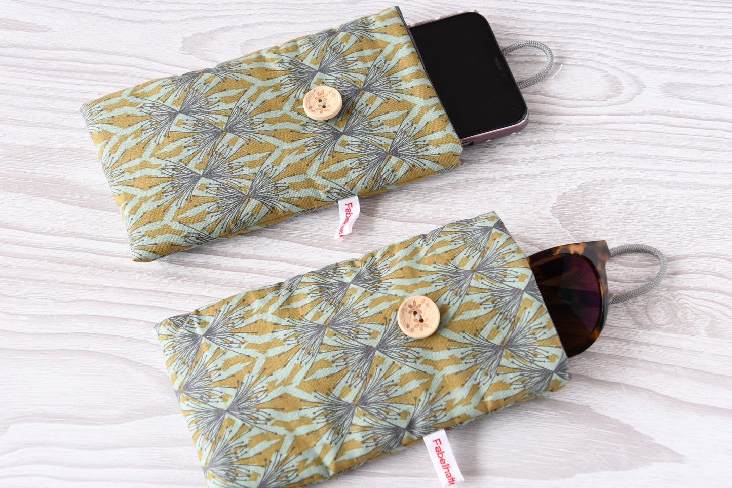 Zwei handgenähte Stofftaschen von Fabelhafte Werkstatt nebeneinander: Eine genutzt als schützende Handyhülle mit Smartphone, die andere als leichtes Brillenetui mit einer Sonnenbrille.