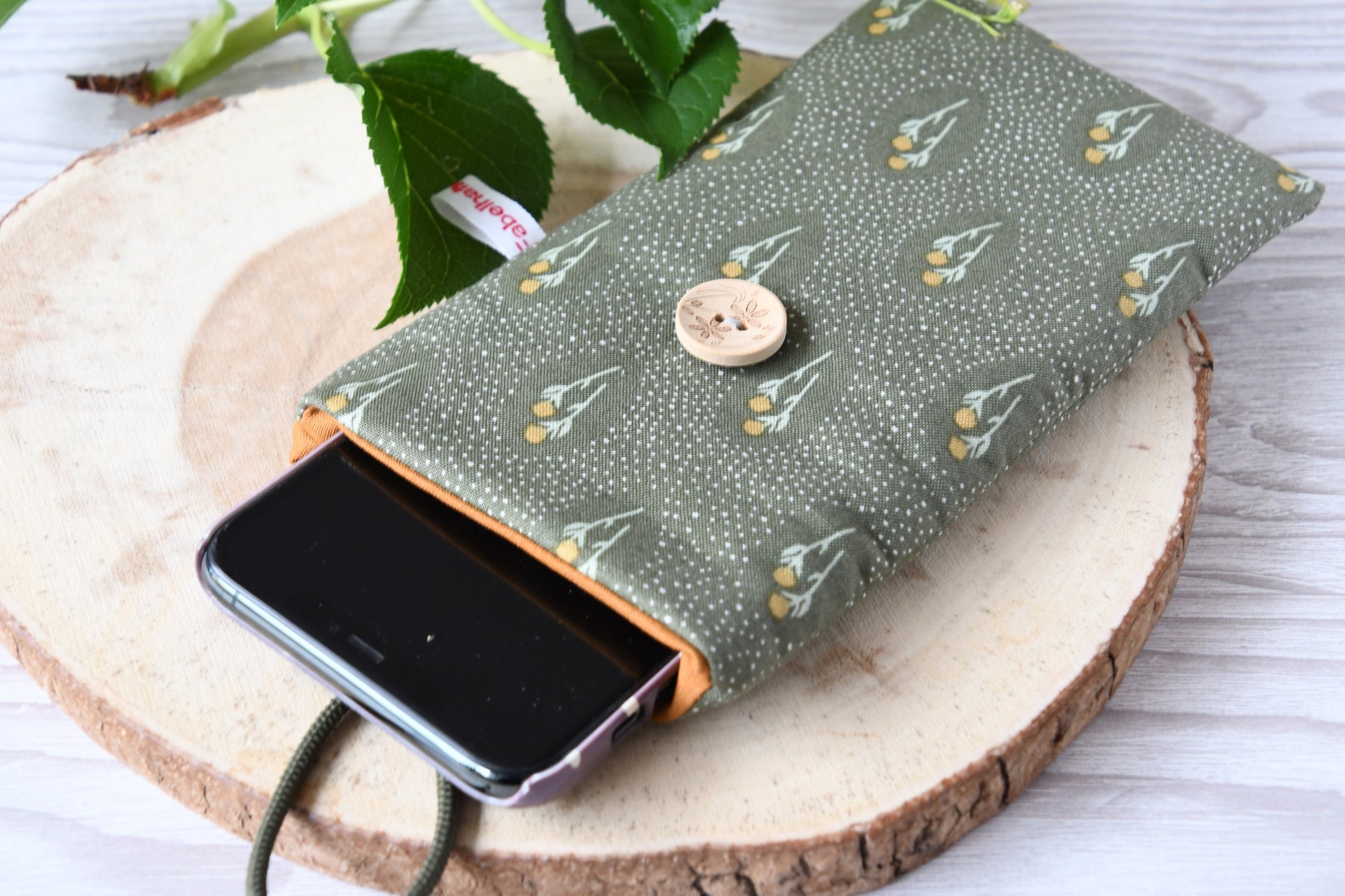 Geöffnete Handyhülle aus geblümtem Stoff mit einem Smartphone, um die Schutzfunktion zu zeigen.