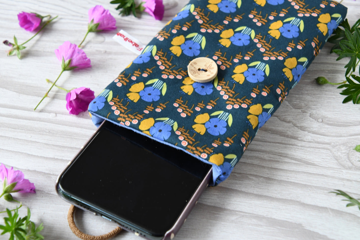 Geöffnete Stoff-Handyhülle mit Blumenmuster und einem Smartphone, das darin sicher vor Kratzern geschützt wird.
