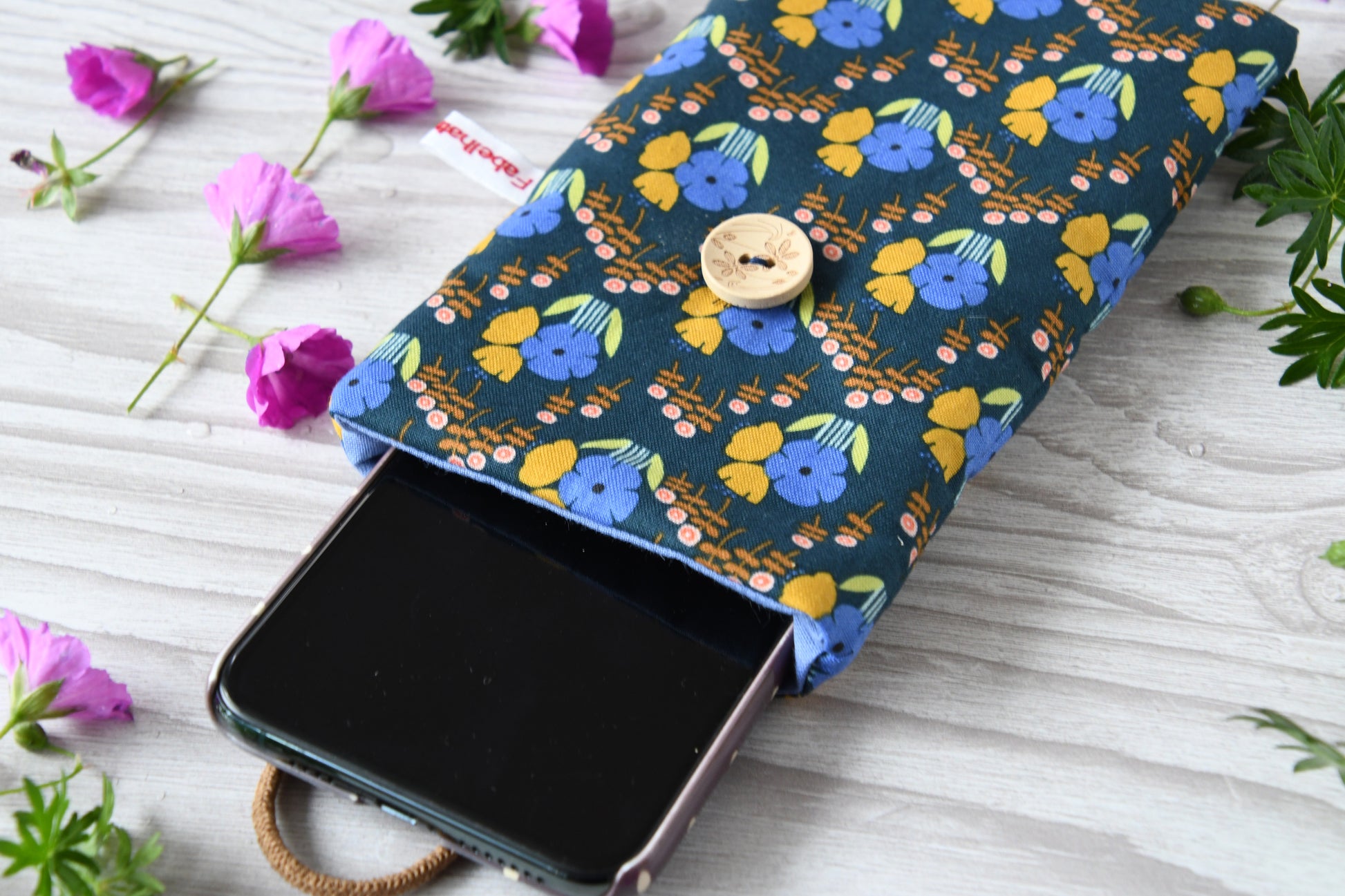 Geöffnete Stoff-Handyhülle mit Blumenmuster und einem Smartphone, das darin sicher vor Kratzern geschützt wird.