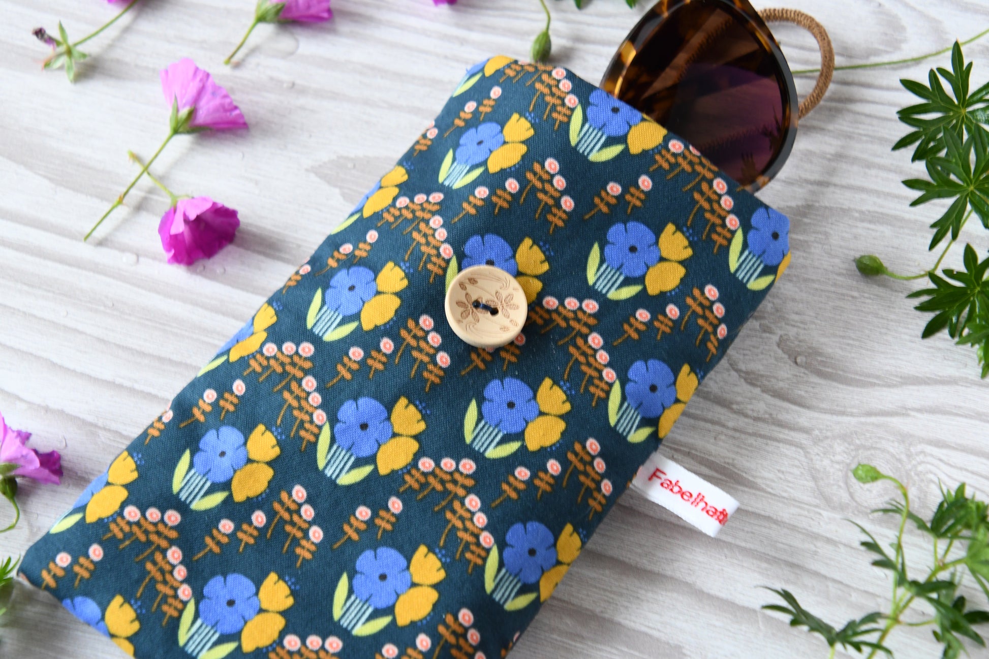 Nahaufnahme des floralen Baumwollstoffes mit Knopf und Gummiband-Verschluss der Fabelhaften Werkstatt.