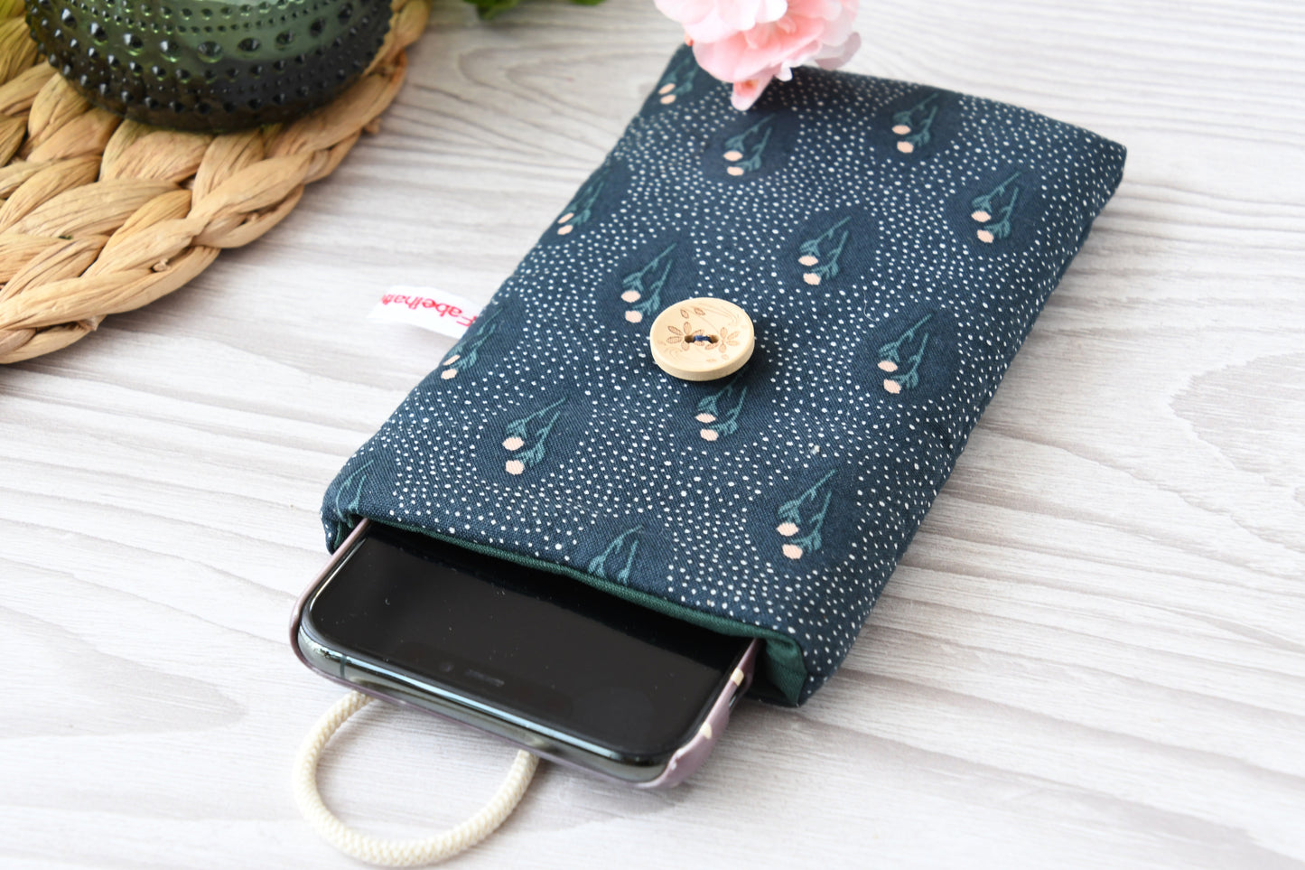 Geöffnete Stoff-Handyhülle mit Blumenmuster und einem Smartphone, das darin sicher vor Kratzern geschützt wird.