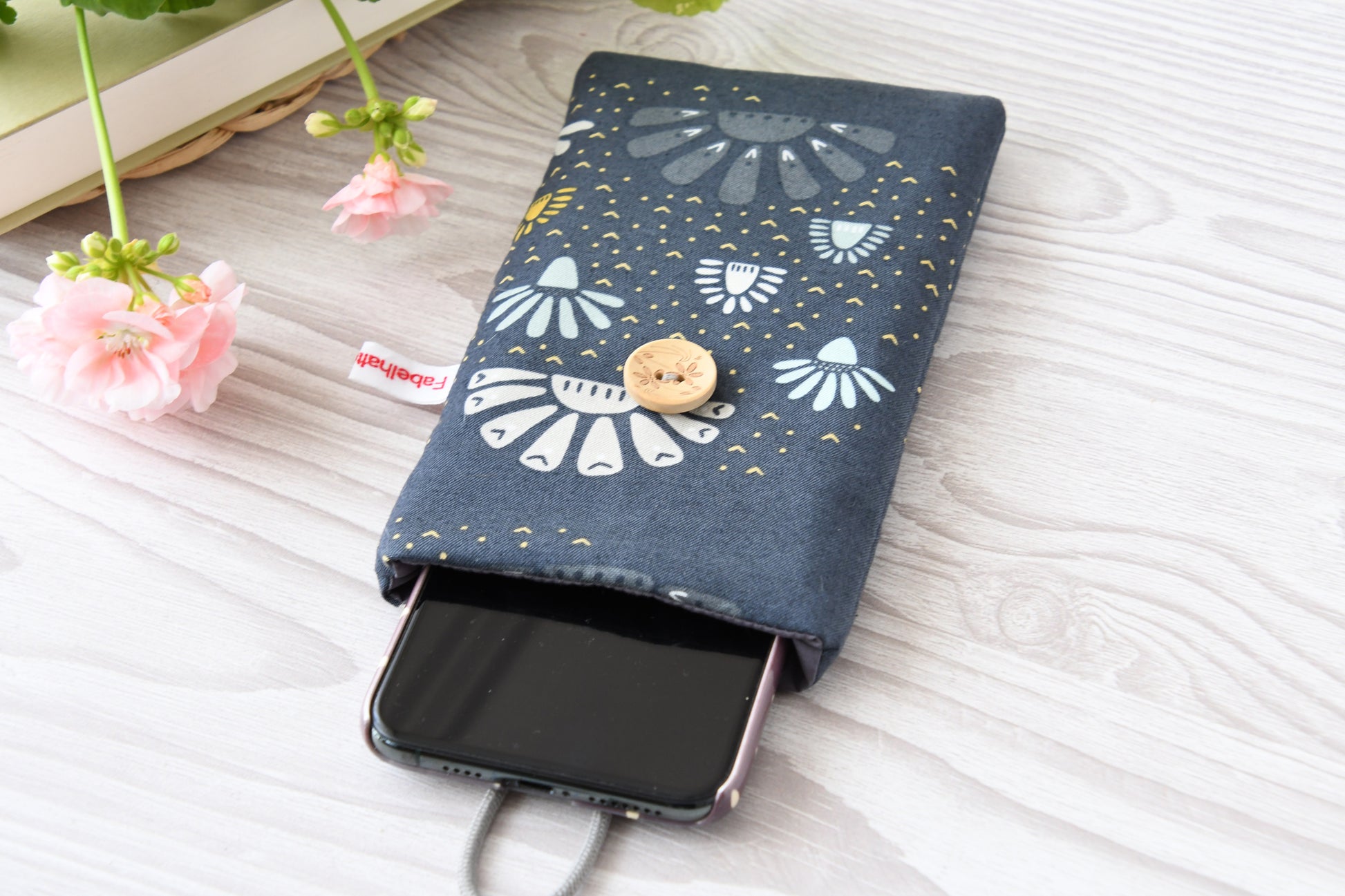 Geöffnete Stoff-Handyhülle mit Blumenmuster und einem Smartphone, das darin sicher vor Kratzern geschützt wird.