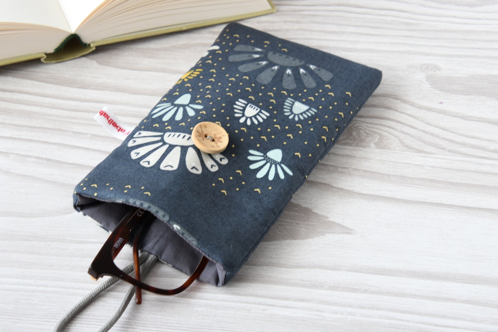 Geöffnete Stoff-Handyhülle mit Blumenmuster und einer Brille, das darin sicher vor Kratzern geschützt wird.