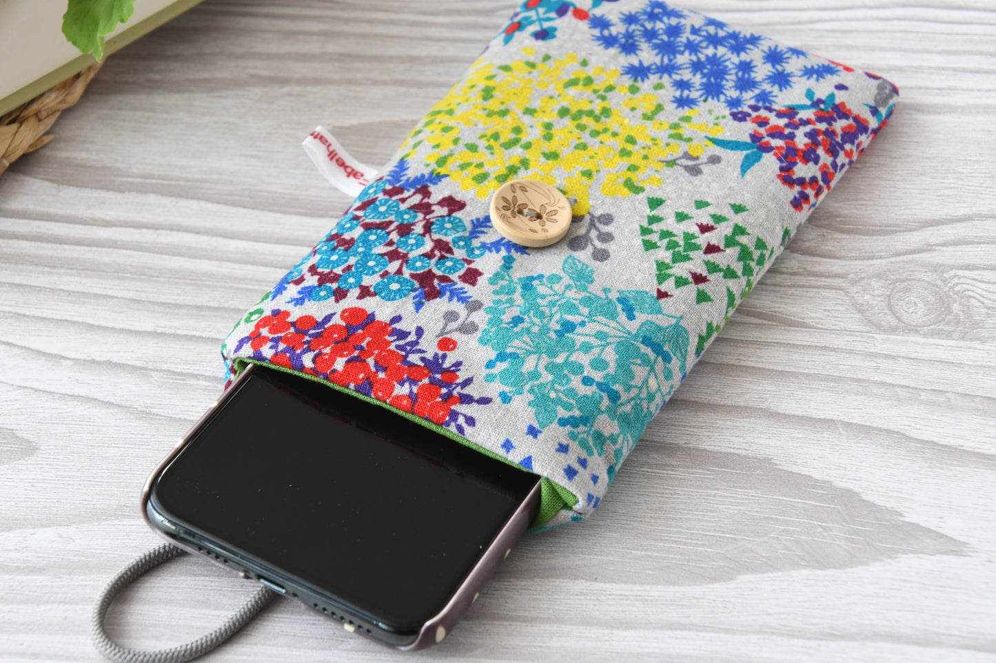 Geöffnete Handyhülle aus geblümtem Stoff mit einem Smartphone, um die Schutzfunktion zu zeigen.