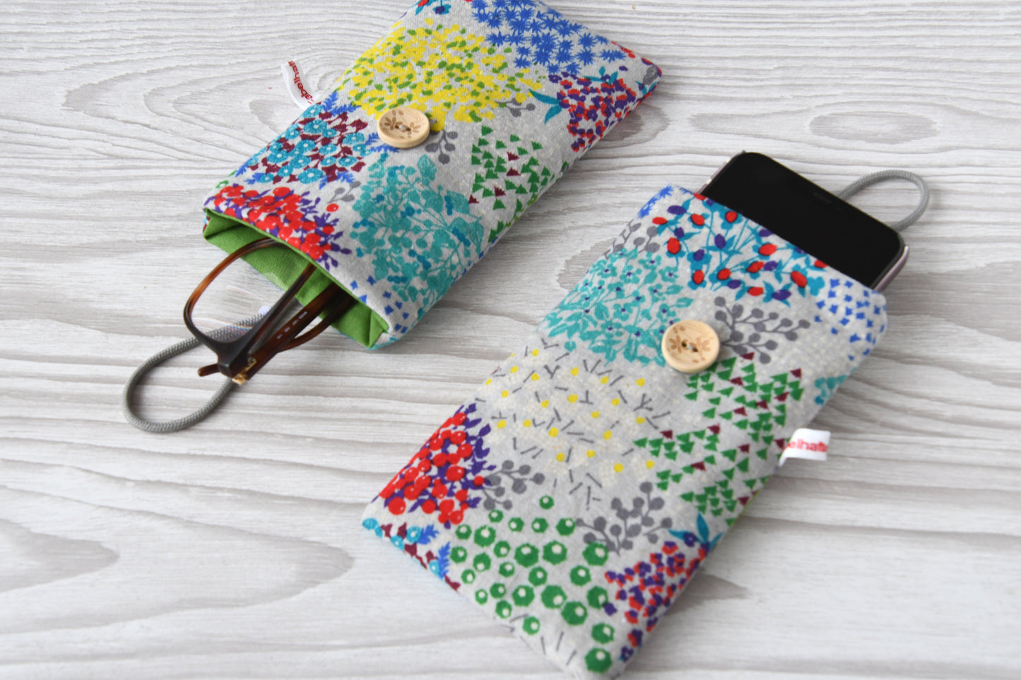 Zwei weich gepolsterte Alltagshelfer von Fabelhafte Werkstatt im Vergleich: Handytasche mit Smartphone und Brillenetui mit Brille nebeneinander liegend.