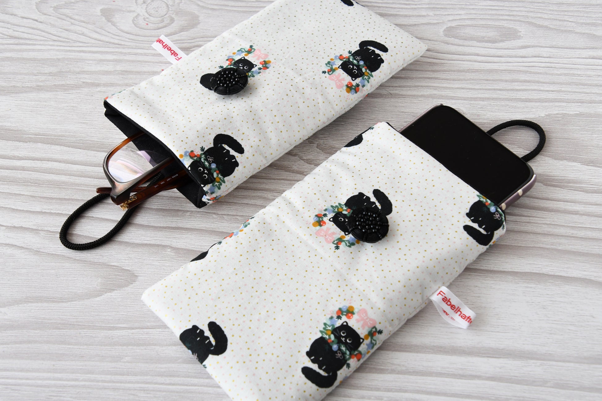 Zwei handgenähte Stofftaschen von Fabelhafte Werkstatt nebeneinander: Eine genutzt als schützende Handyhülle mit Smartphone, die andere als leichtes Brillenetui mit einer Sonnenbrille.