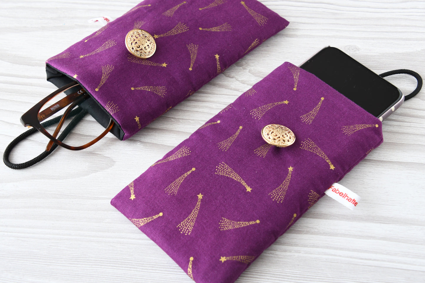 Zwei handgenähte Stofftaschen mit goldenen Sternschnuppen von Fabelhafte Werkstatt nebeneinander: Eine genutzt als Handyhülle mit Smartphone, die andere als Brillenetui mit Brille.