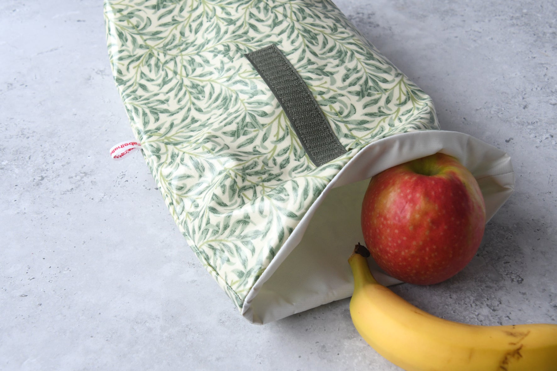 Geöffneter Lunchbag mit Olivenzweigen von Fabelhaftewerkstatt, gefüllt mit gesundem Obst für unterwegs.