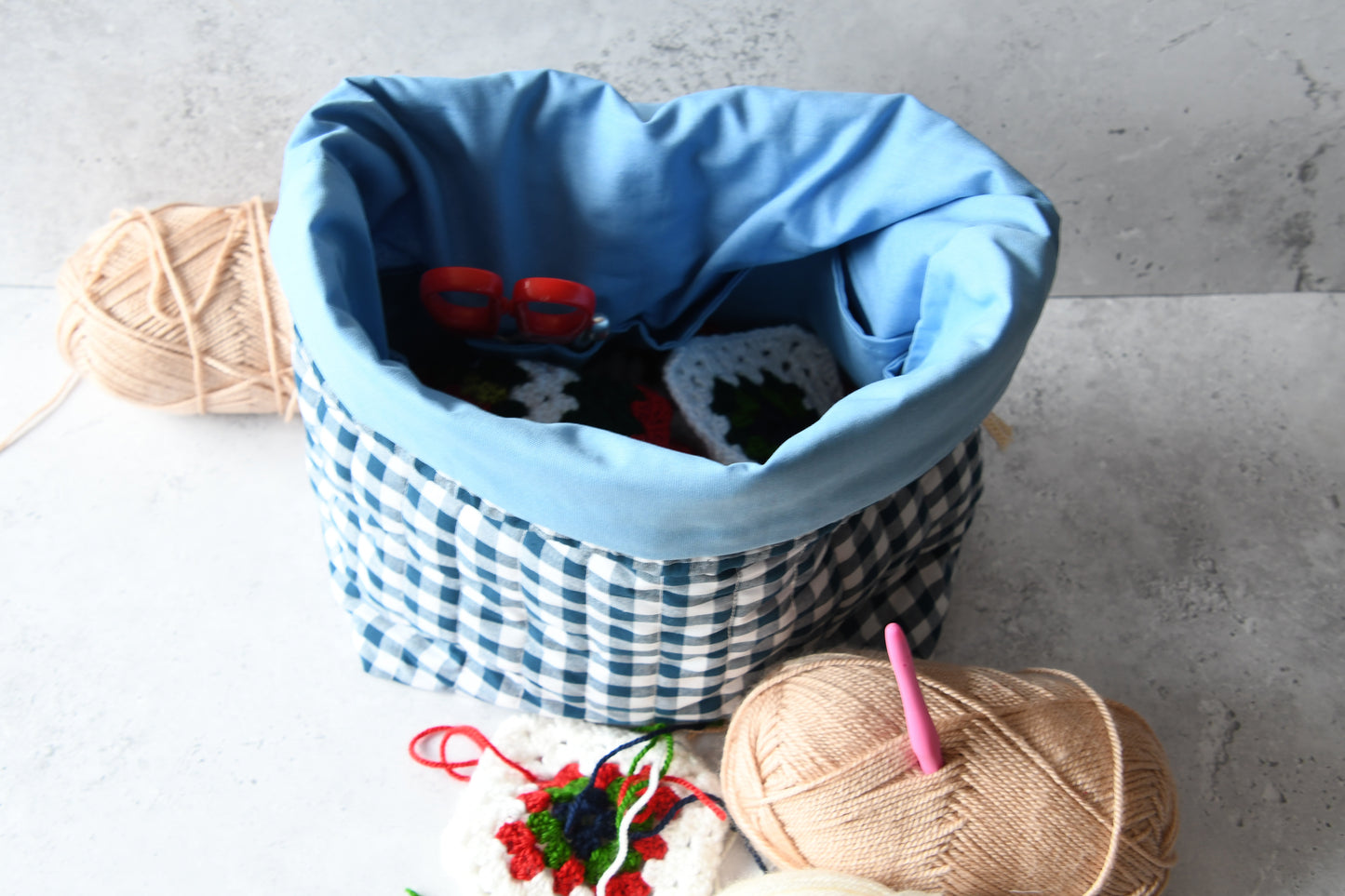 Die blaue Projekttasche kariert, gefüllt mit Wolle und einer Stricknadel, bereit für den nächsten Handarbeitsabend.