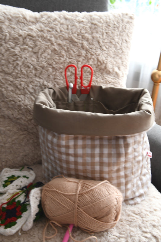 Die karierte Projekttasche in Beige „in Action“, gefüllt mit mehreren Wollknäueln, einem Häkelprojekt und einer Schere.