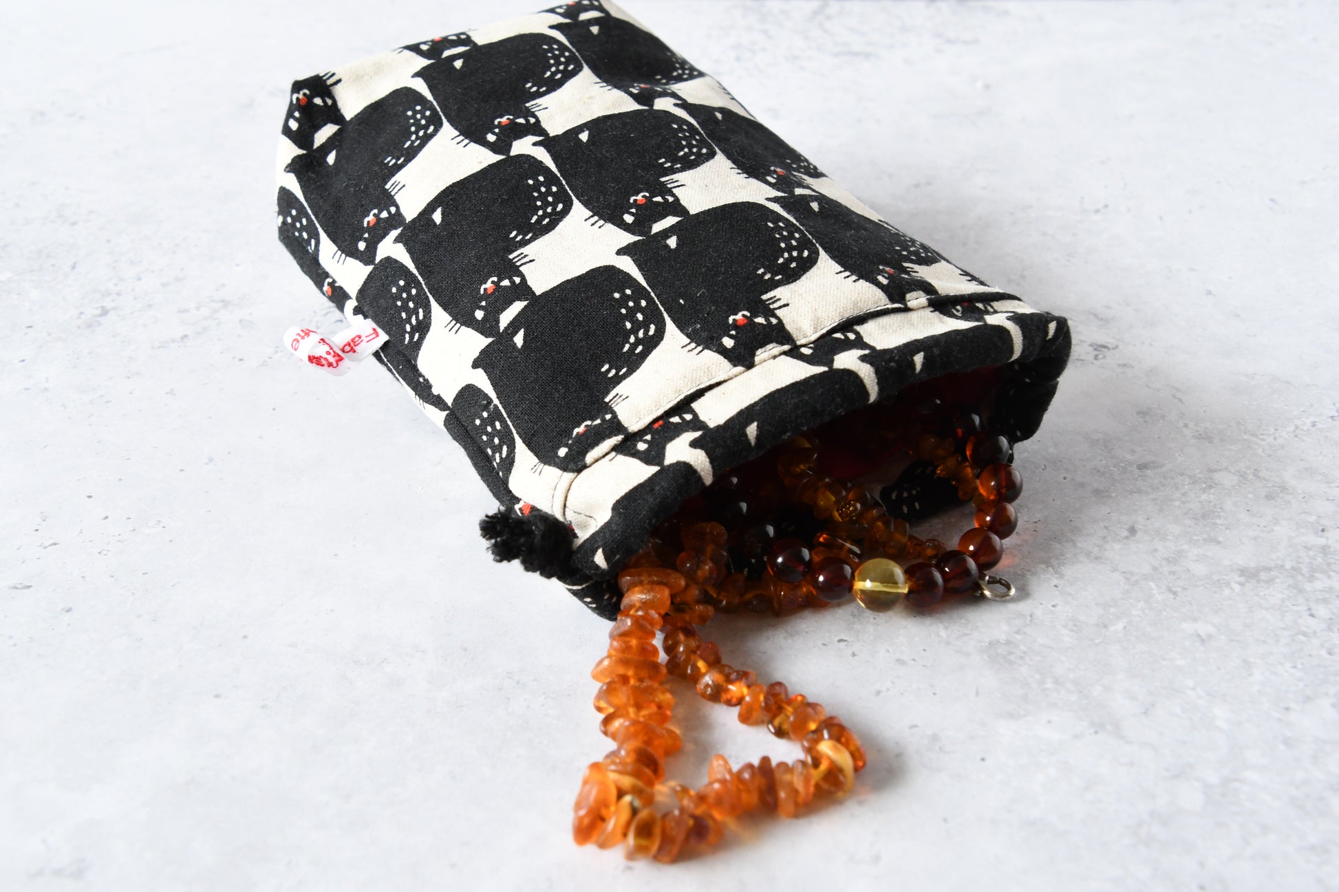 Geöffneter Stoffbeutel mit Katzenmotiv und Kordelzug, gefüllt mit Schmuck, handgemacht für mehr Ordnung.