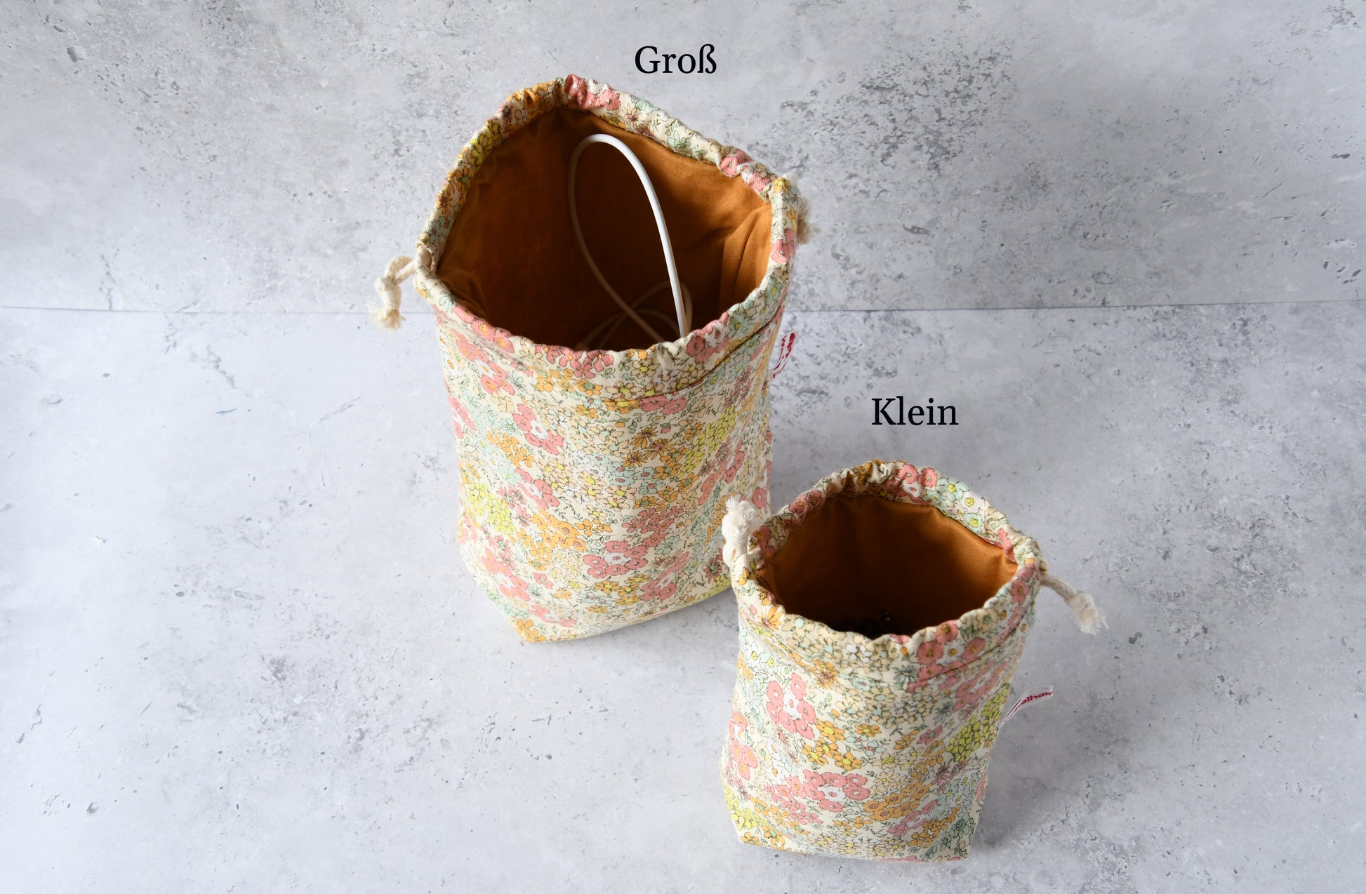 Größenvergleich der handgemachten Kinchaku-Beutel mit rosafarbenem Streublumen-Muster von Fabelhafte Werkstatt: Das kleine und große Modell nebeneinander.