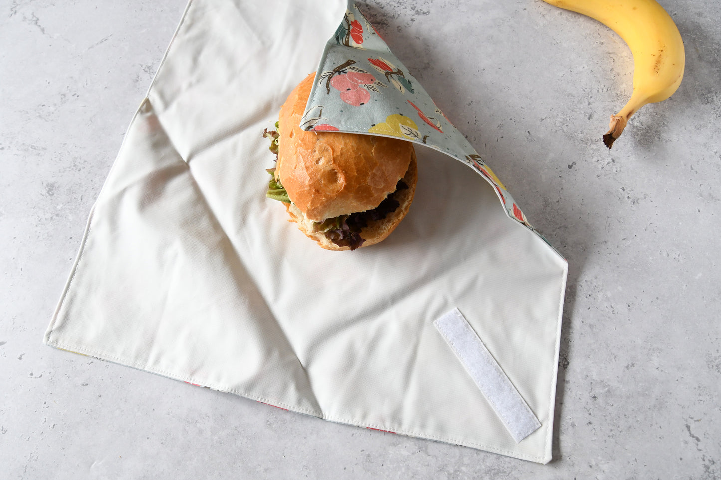 Belegtes Brötchen im geöffneten Sandwich Wrap, eine Seite ist bereits eingeklappt.