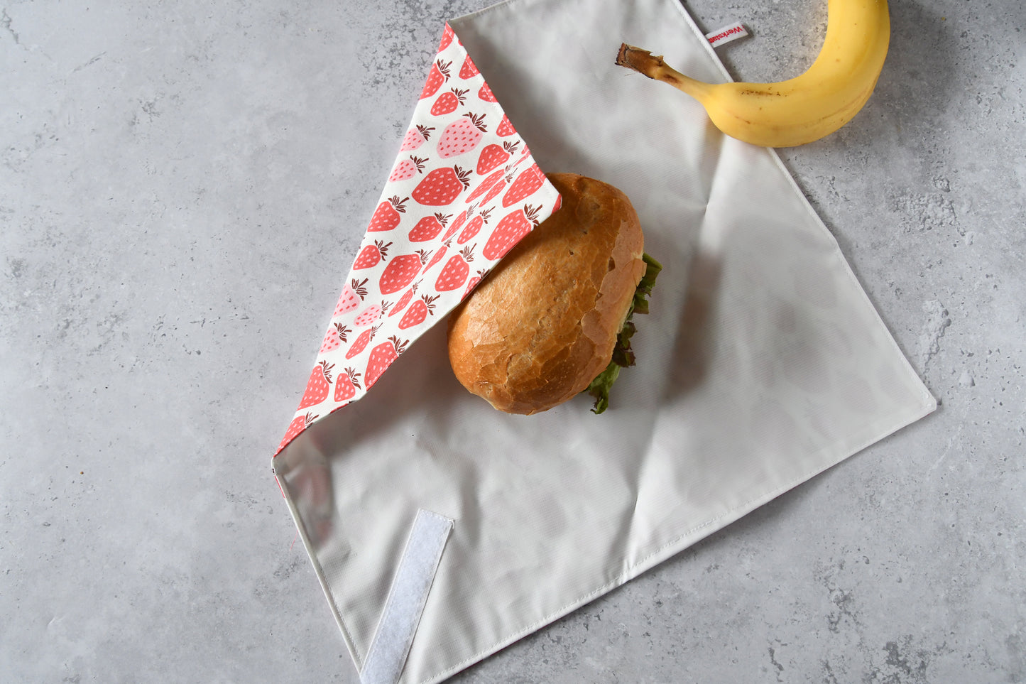 Schritt-für-Schritt-Anleitung: Ein belegtes Brötchen liegt auf dem aufgeklappten Sandwich Wrap, der von einer Seite eingeschlagen wird.