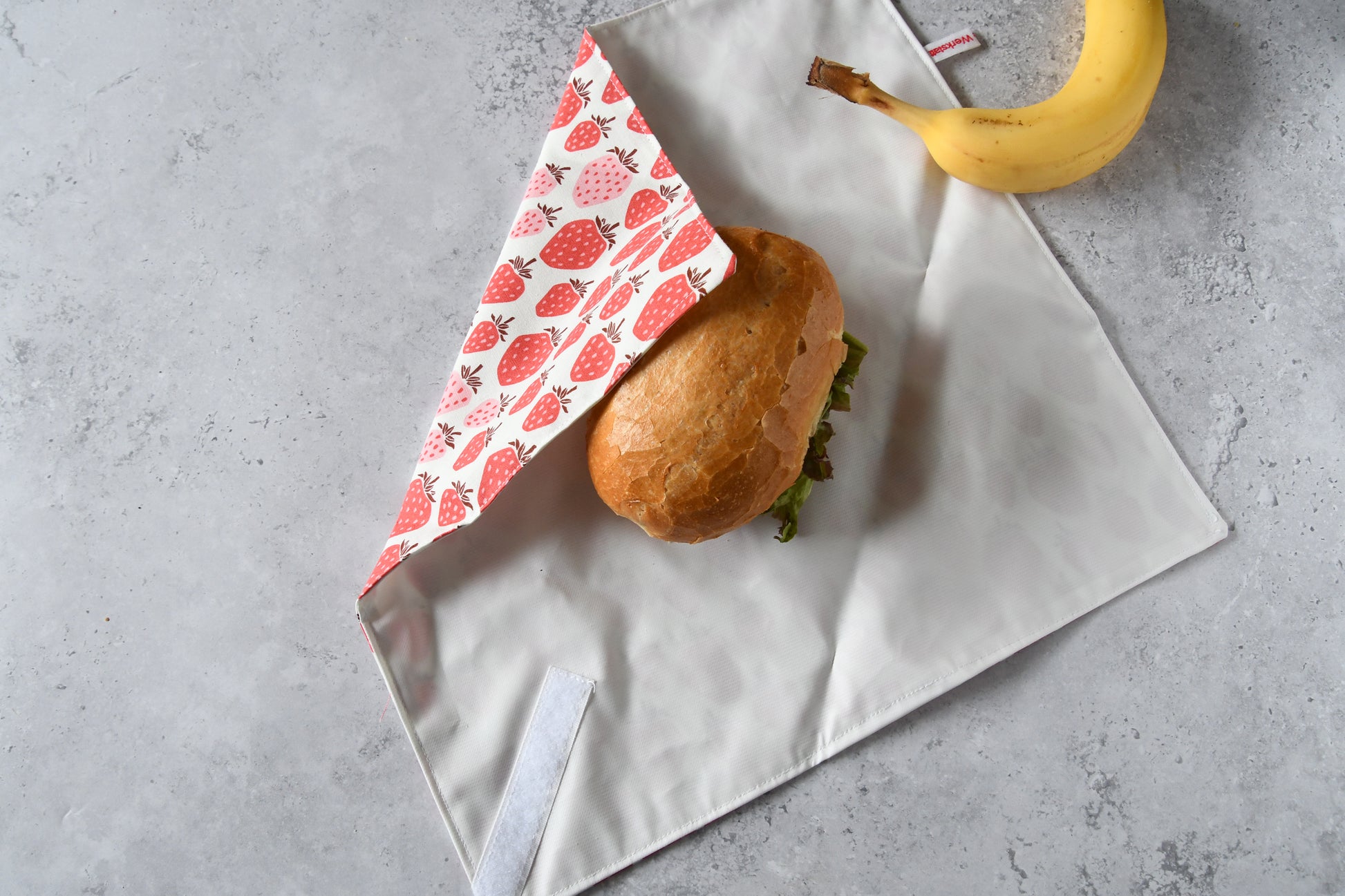 Schritt-für-Schritt-Anleitung: Ein belegtes Brötchen liegt auf dem aufgeklappten Sandwich Wrap, der von einer Seite eingeschlagen wird.