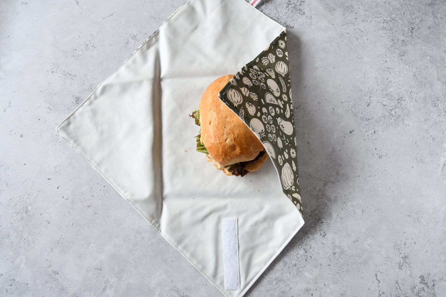 Belegtes Brötchen im geöffneten Sandwich Wrap, eine Seite ist bereits eingeklappt.