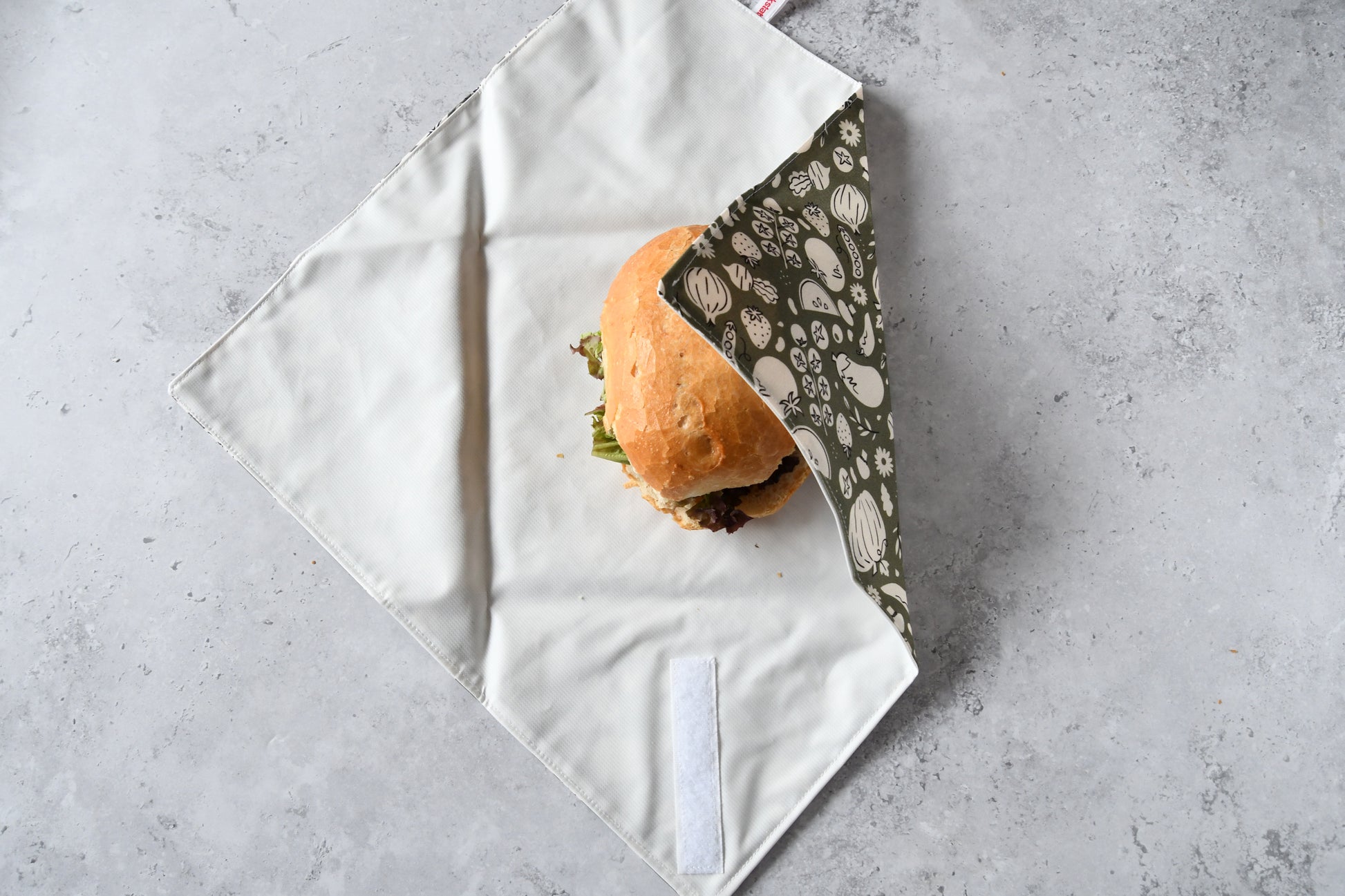 Belegtes Brötchen im geöffneten Sandwich Wrap, eine Seite ist bereits eingeklappt.
