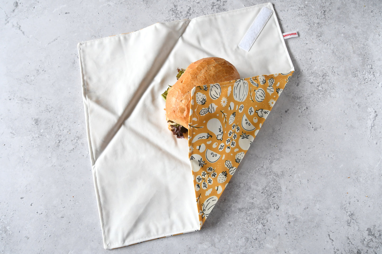 Belegtes Brötchen im geöffneten Sandwich Wrap, eine Seite ist bereits eingeklappt.