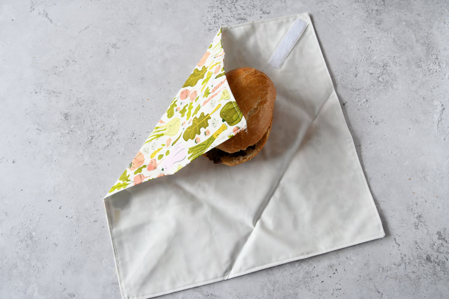 Schritt-für-Schritt-Anleitung: Ein belegtes Brötchen liegt auf dem aufgeklappten Sandwich Wrap, der von einer Seite eingeschlagen wird.