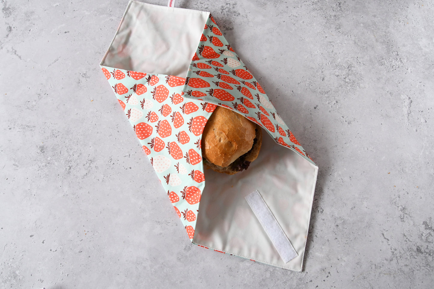 Wiederverwendbare Pausenbrot-Verpackung von Fabelhafte Werkstatt, zu zwei Dritteln um ein Brötchen gefaltet.