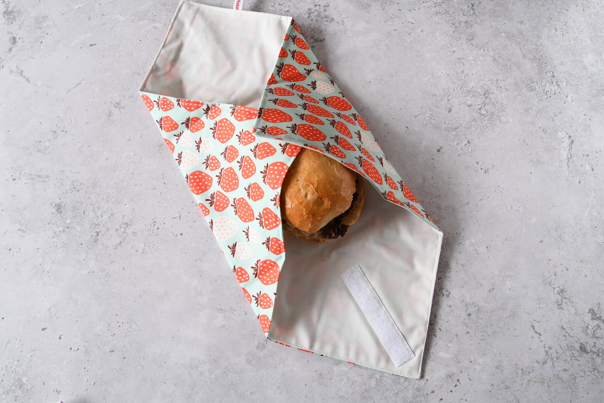 Wiederverwendbare Pausenbrot-Verpackung von Fabelhafte Werkstatt, zu zwei Dritteln um ein Brötchen gefaltet.