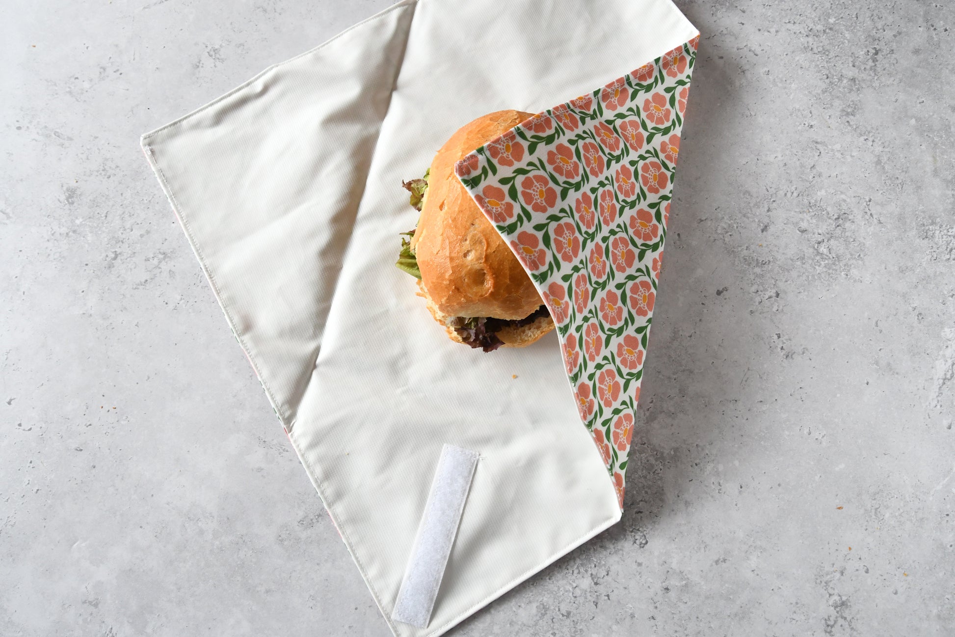 Belegtes Brötchen im geöffneten Sandwich Wrap, eine Seite ist bereits eingeklappt.