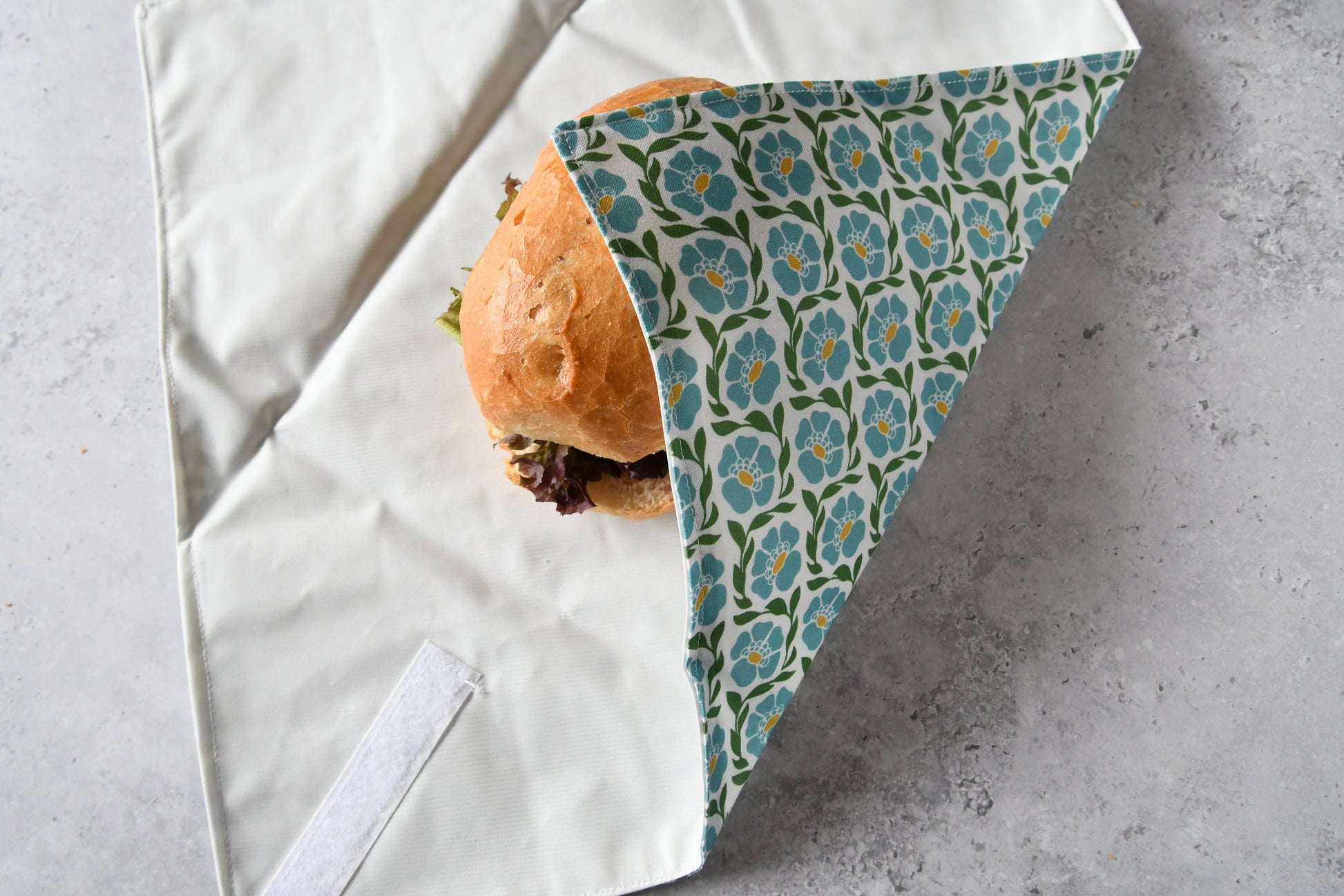 Schritt-für-Schritt-Anleitung: Ein belegtes Brötchen liegt auf dem aufgeklappten Sandwich Wrap, der von einer Seite eingeschlagen wird.