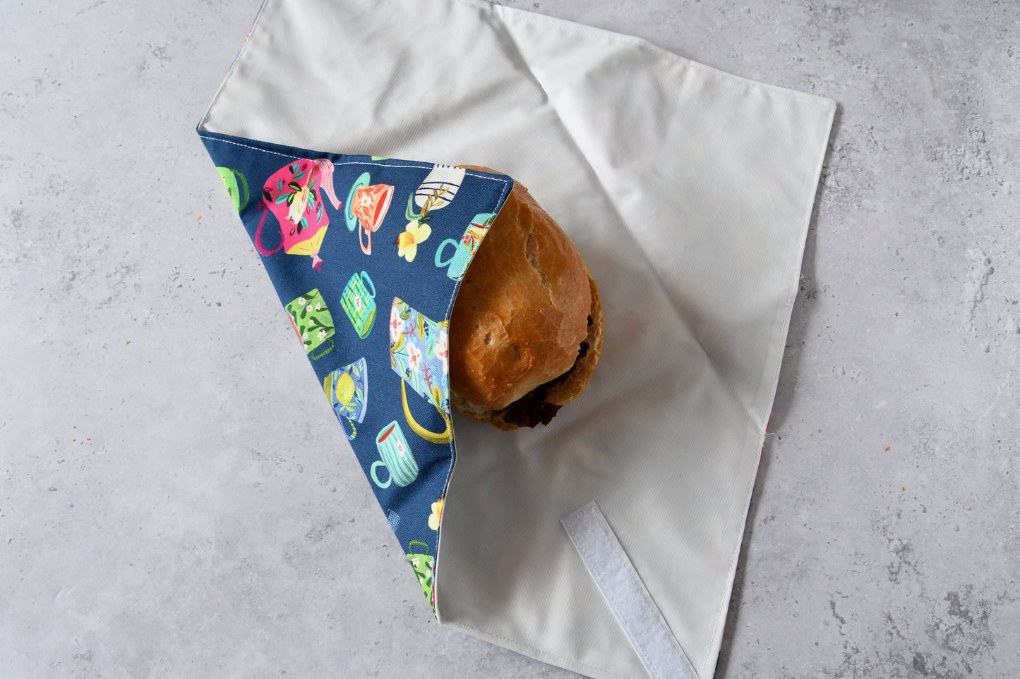 Belegtes Brötchen im geöffneten Sandwich Wrap, eine Seite ist bereits eingeklappt.