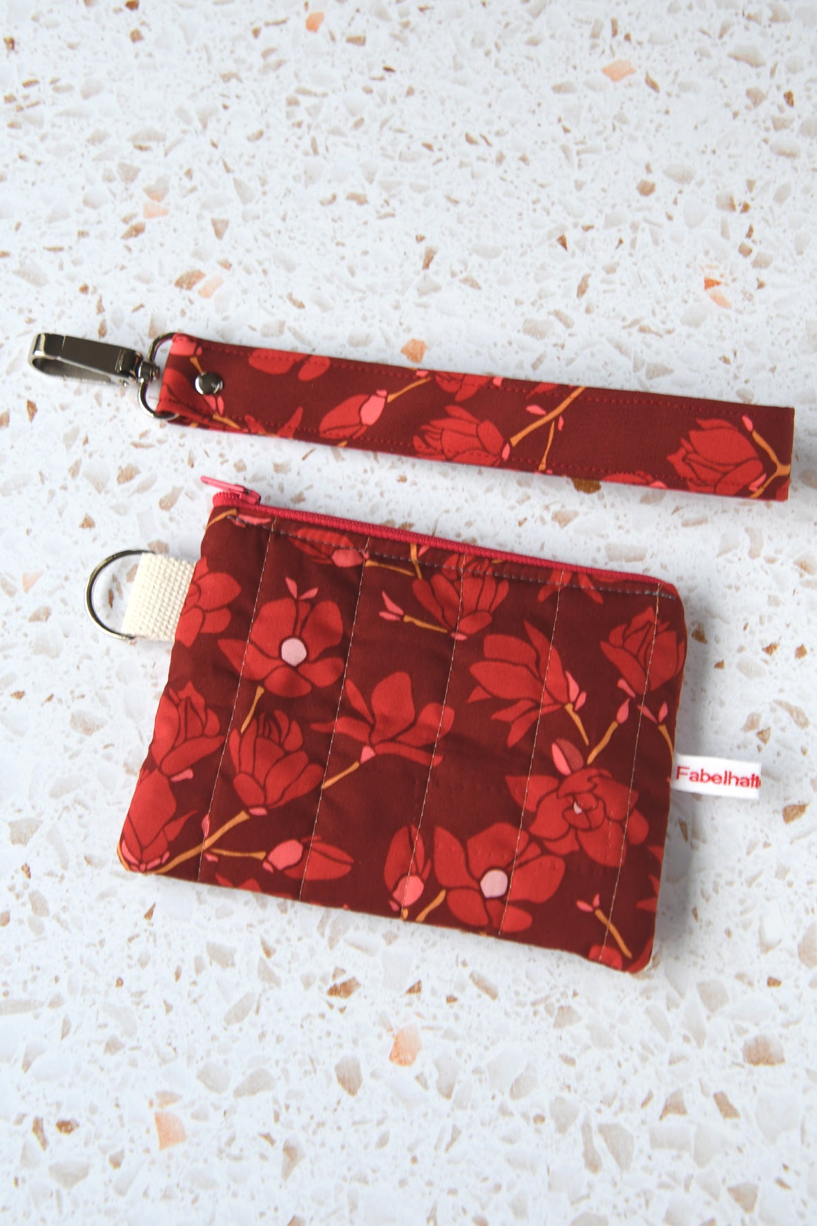 Draufsicht auf das geschlossene Schlüsseltäschchen "Magnolia" mit dem darüberliegenden, optionalen Schlüsselband im gleichen Design