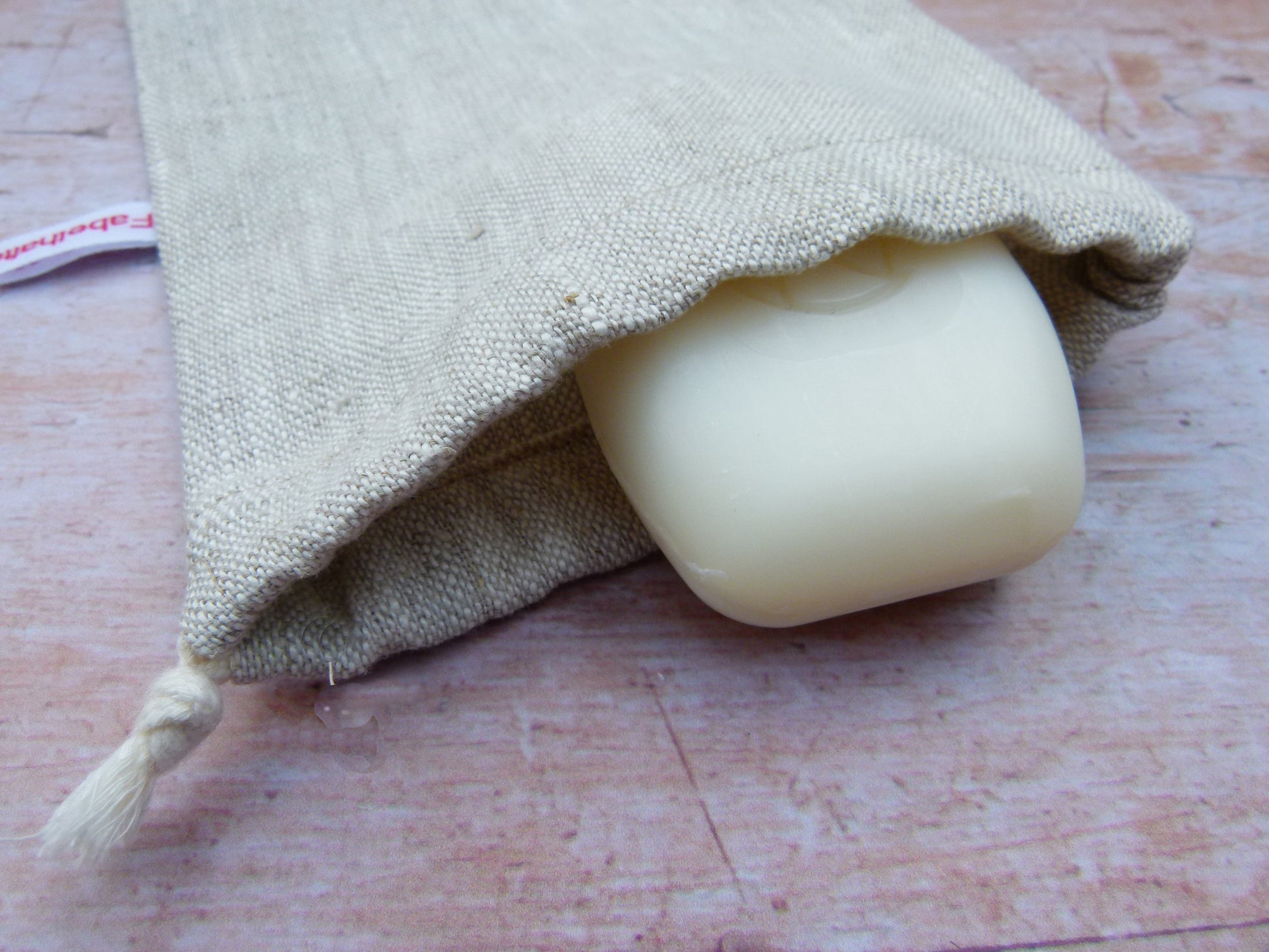 Handgenähtes Seifensäckchen von Fabelhaftewerkstatt aus reinem Leinen in der Farbe Natur, aus dem ein Stück feste Duschseife herausschaut.