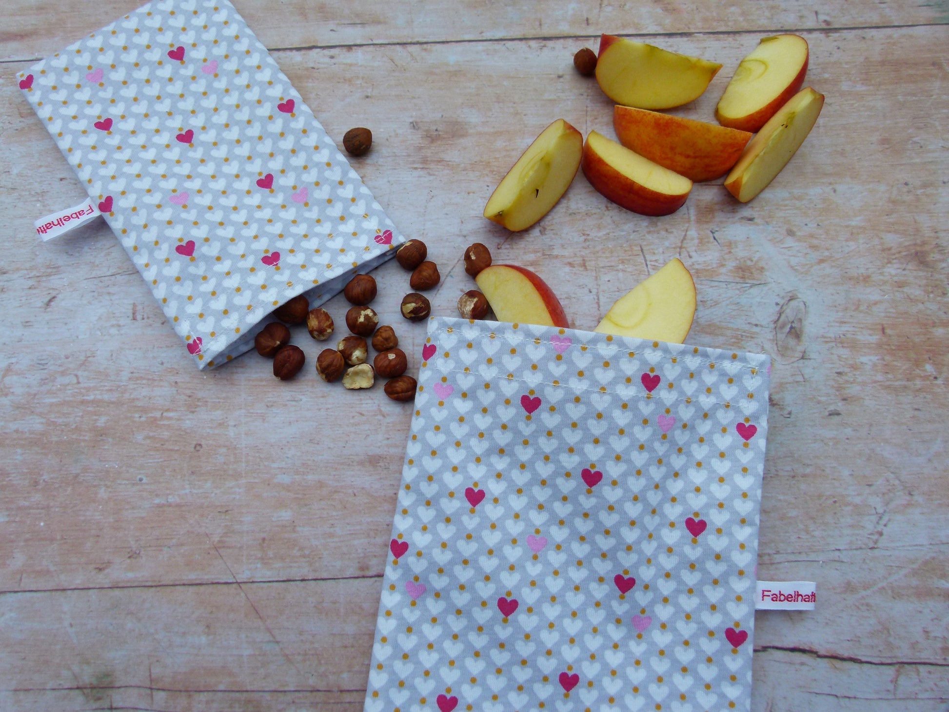 Wiederverwendbare Snackbeutel aus Stoff im Größenvergleich: Nachhaltige, lebensmittelechte Snackbags für unterwegs, befüllt mit gesunden Snacks wie Apfelstücken und Nüssen.