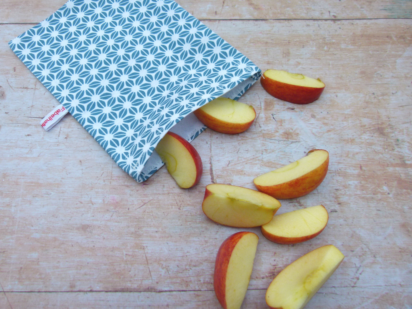Handgenähter, nachhaltiger Snackbag von Fabelhaftewerkstatt aus lebensmittelechtem Stoff, geöffnet und befüllt mit Apfelscheiben auf einem Küchentisch.