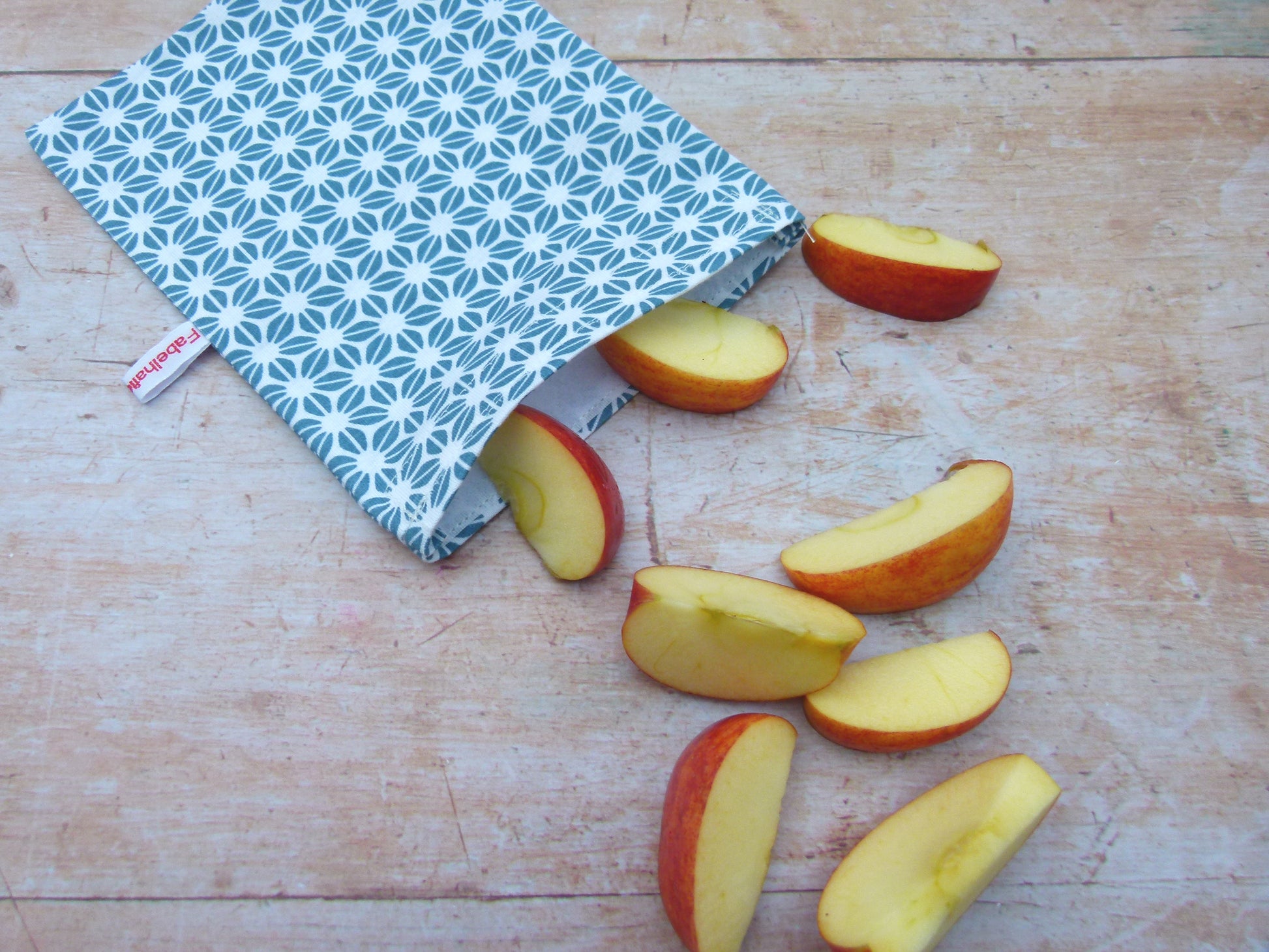 Handgenähter, nachhaltiger Snackbag von Fabelhaftewerkstatt aus lebensmittelechtem Stoff, geöffnet und befüllt mit Apfelscheiben auf einem Küchentisch.