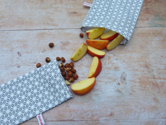 Wiederverwendbare Snackbeutel aus Stoff im Größenvergleich: Nachhaltige, lebensmittelechte Snackbags für unterwegs, befüllt mit gesunden Snacks wie Apfelstücken und Nüssen.