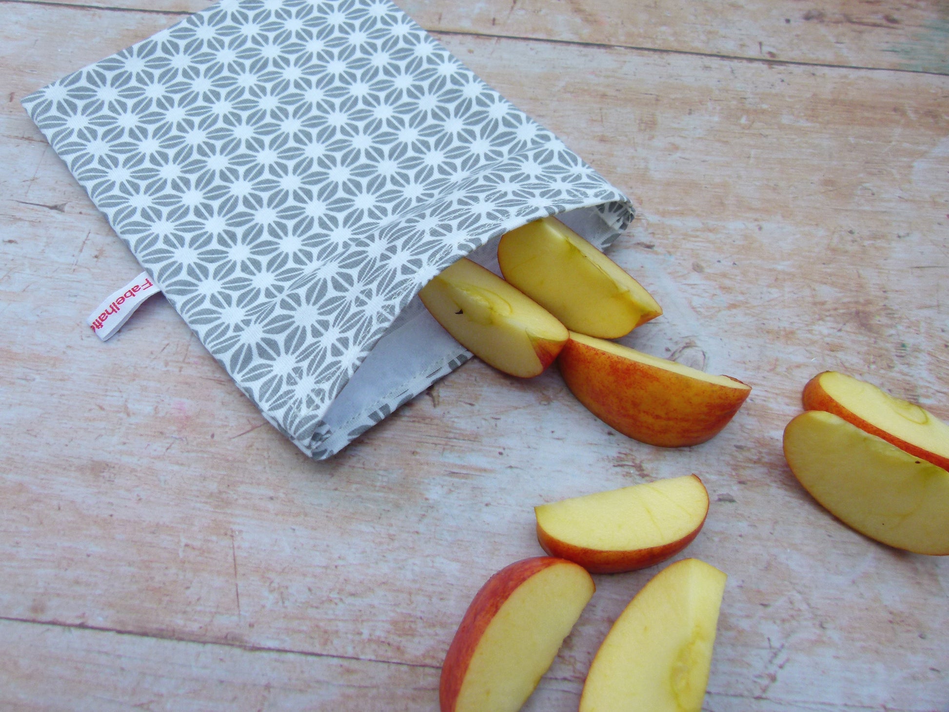 Handgenähter, nachhaltiger Snackbag von Fabelhaftewerkstatt aus lebensmittelechtem Stoff, geöffnet und befüllt mit Apfelscheiben auf einem Küchentisch.