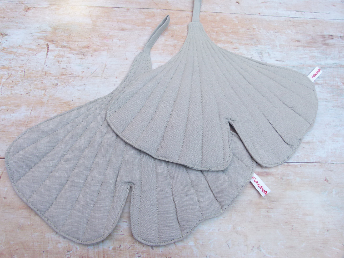 Ein Set aus zwei handgenähten Topflappen in der Form eines Ginkgoblattes, gefertigt aus hellgrauen Leinen.  