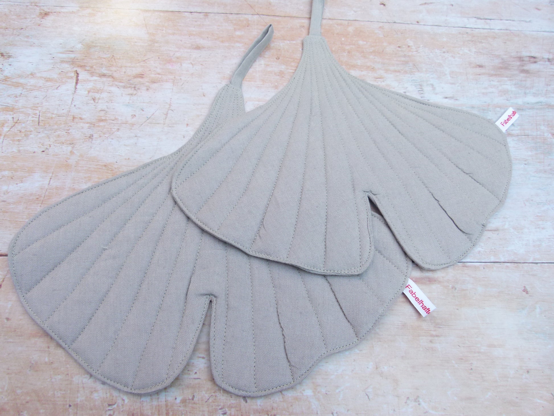 Ein Set aus zwei handgenähten Topflappen in der Form eines Ginkgoblattes, gefertigt aus hellgrauen Leinen.  