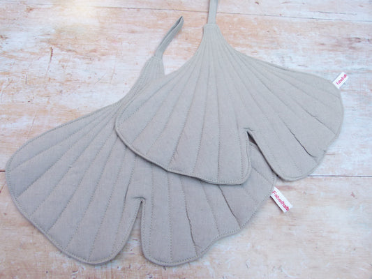 Ein Set aus zwei handgenähten Topflappen in der Form eines Ginkgoblattes, gefertigt aus hellgrauen Leinen.  
