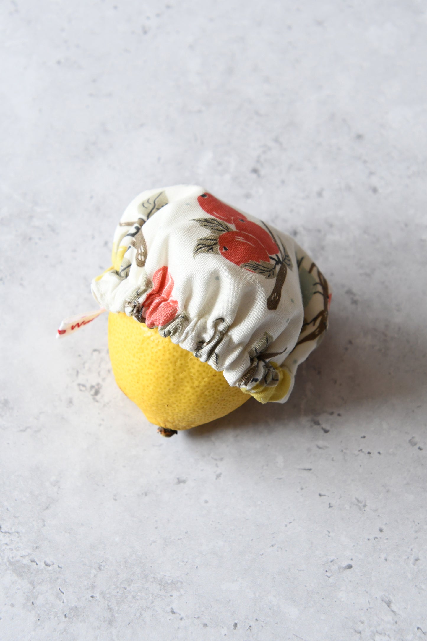 Kleine elfenbeinfarbene Schüsselhaube mit Obstzweige-Motiv, gezogen über eine angeschnittene Zitrone.