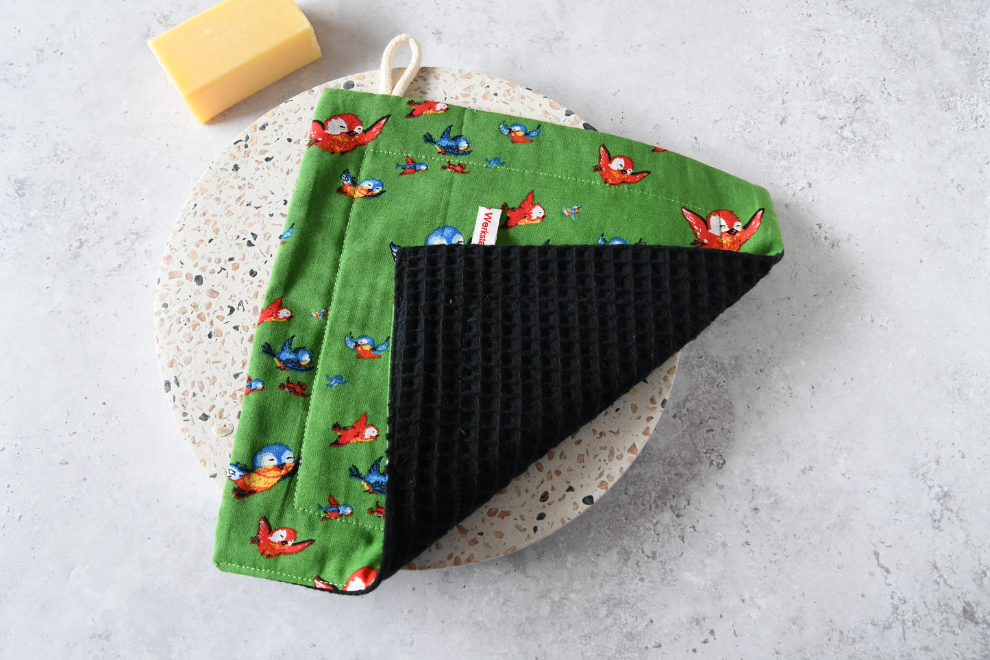 Nahaufnahme des Spültuchs mit umgeklappter Ecke: Vorderseite mit Motiv und saugstarke Rückseite aus Waffelpique.