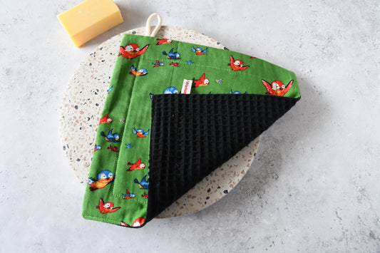 Nahaufnahme des Spültuchs mit umgeklappter Ecke: Vorderseite mit Motiv und saugstarke Rückseite aus Waffelpique.